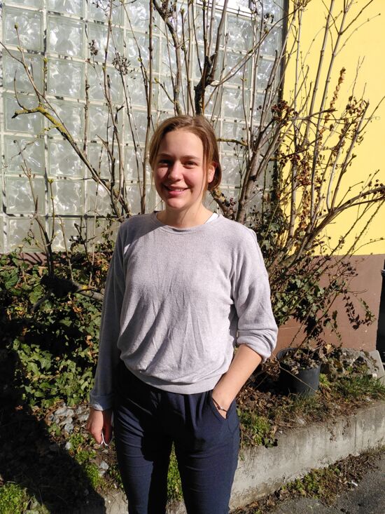 Junge Frau steht vor einem Busch in der Sonne und lächelt